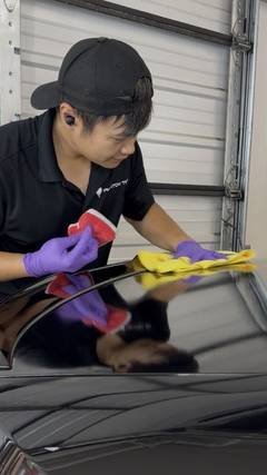 Phantom Tint technician in a black cap and purple gloves applying ceramic coating to a vehicle